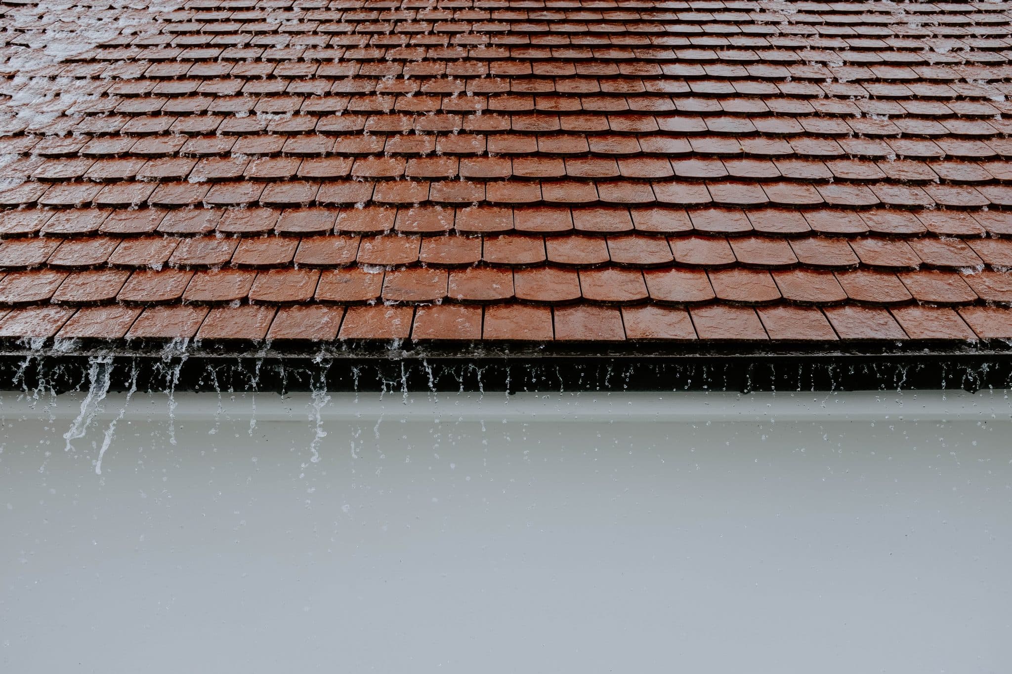 Rainwater drips from a red terracotta tile roof edge against a plain white wall.